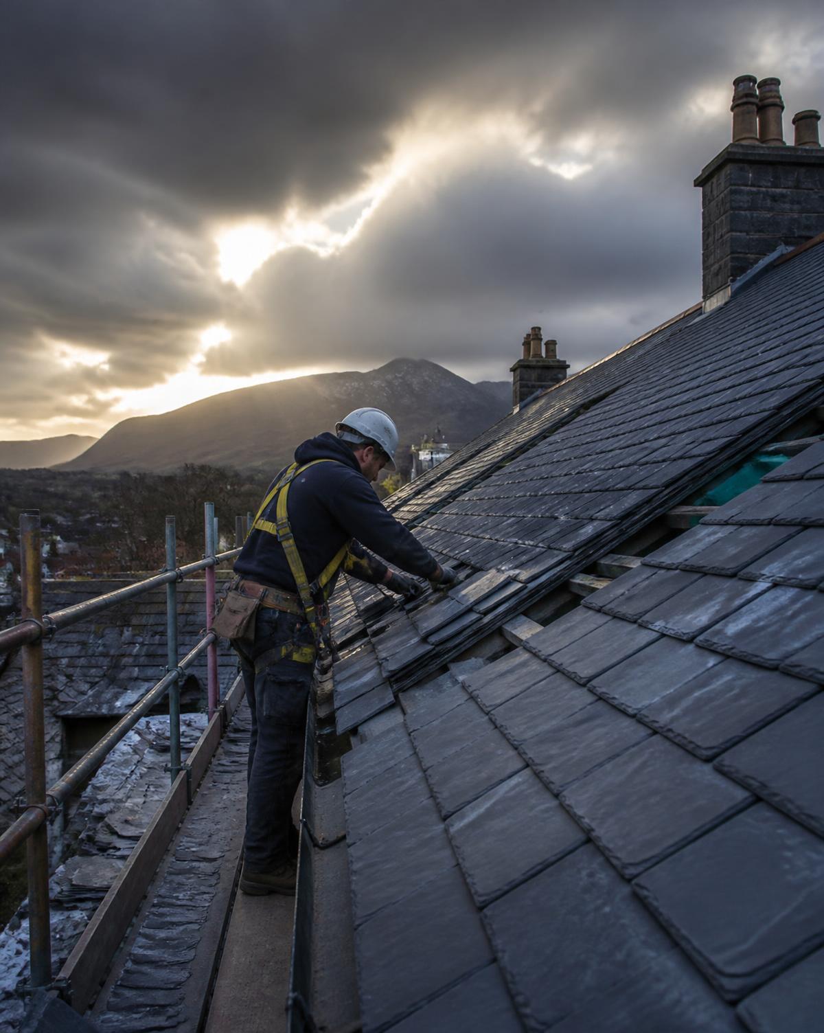 Roofer re-slating a pitched Cumbrian roof from scaffolding at dusk